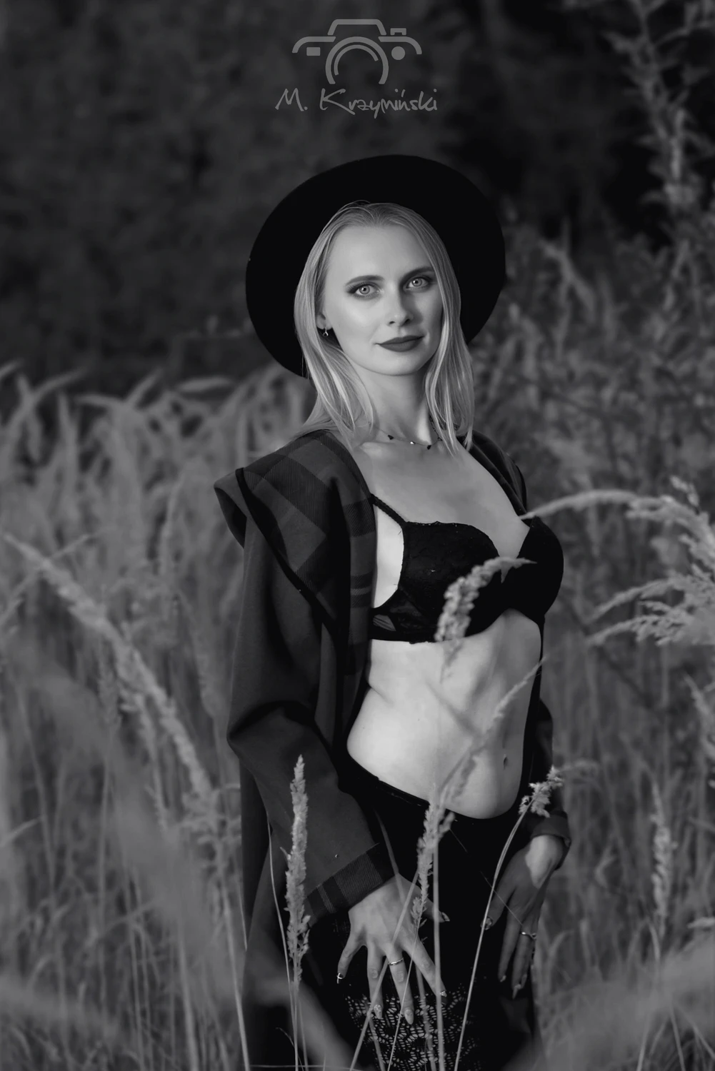 „Płaszcz rozpięty słońcem, cień kapelusza i czerń bielizny, która kradnie spojrzenia pośród wysokich traw.”